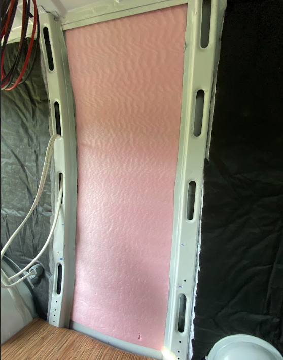 A piece of pink foam insulation board cut to fit an installed between two vertical structural ribs inside a cargo van.