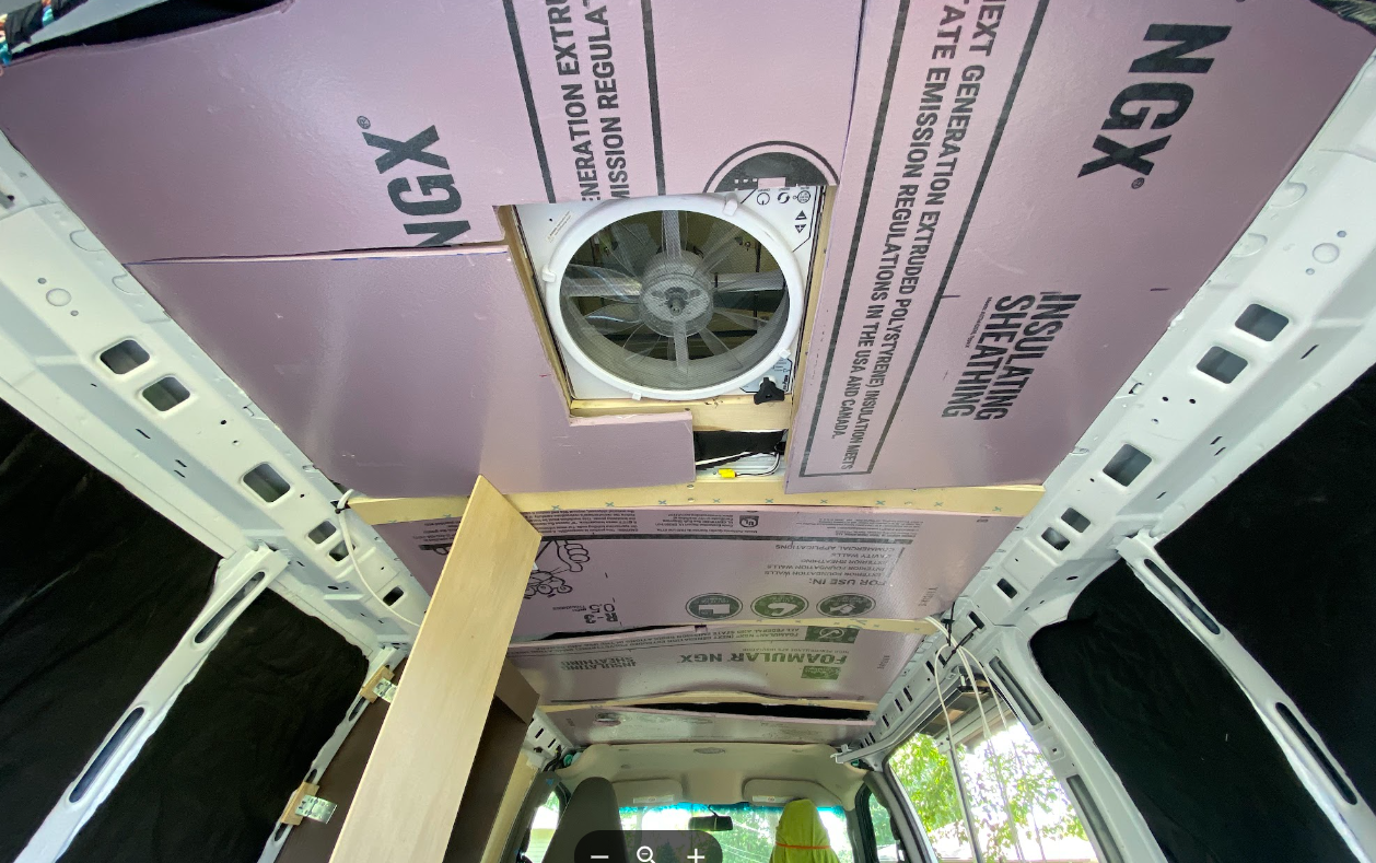 A view of the interior roof of a cargo van, with wood strips between sheets of pink foam insulation.
