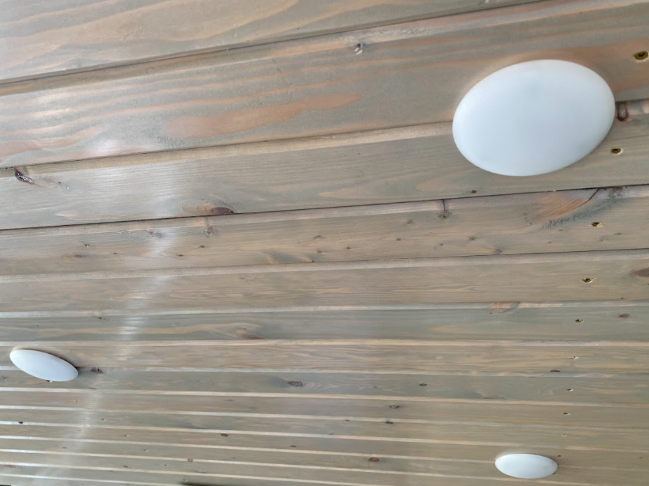 A view toward a wooden ceiling with three small, round white lights installed in it.