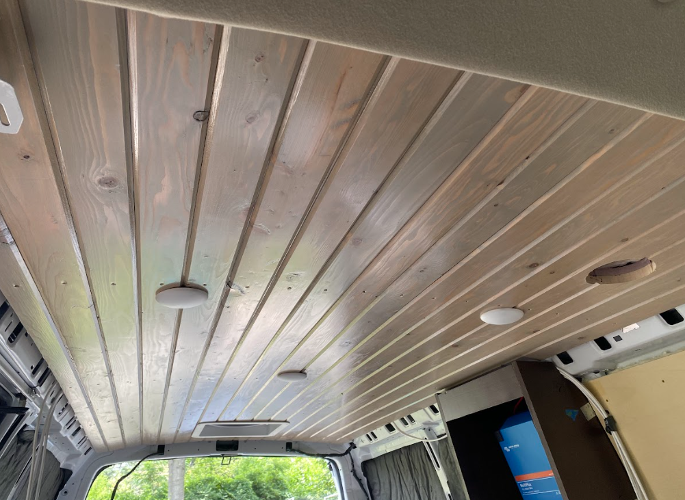 Interior of a cargo van, looking up from the front at a tongue and groove wood ceiling.