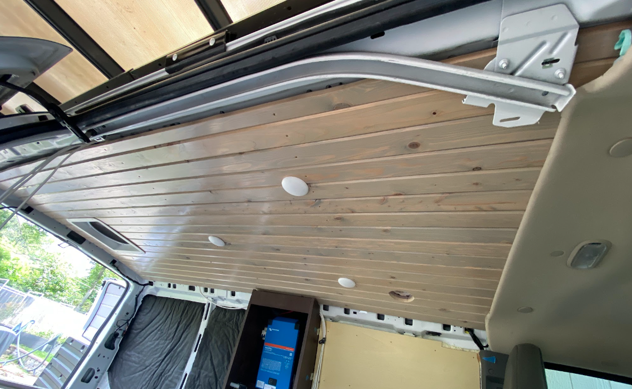 Interior of a cargo van, looking up from the side door at a tongue and groove wood ceiling.
