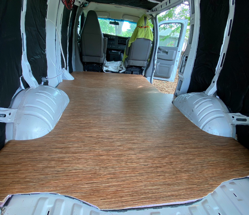 A wood-look vinyl floor cut and applied to the floor of a van; view from rear.