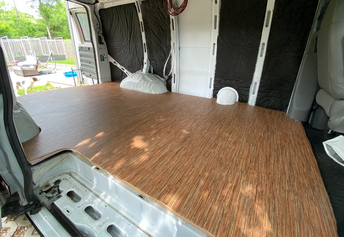 A wood-look vinyl floor cut and applied to the floor of a van; view from side door.