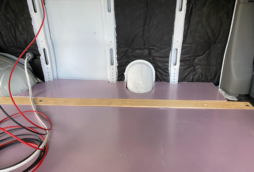 A view inside a cargo van from the side, with the floor lined in pink insulation foam board.
