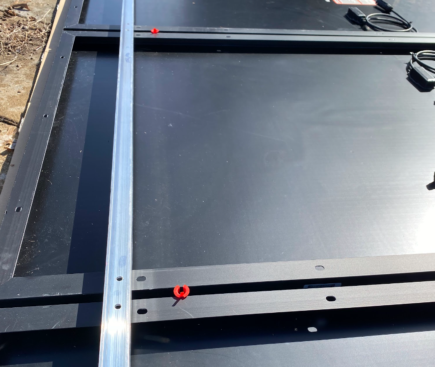 An aluminum U-channel placed on top of solar panels so the holes in the channel are lined up with the holes in the panels.
