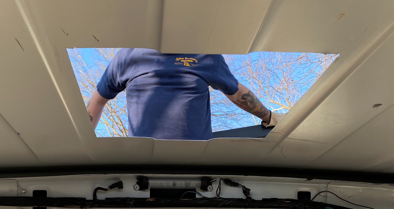 A view from the inside of the cargo van. A person wearing a blue shirt with the words "Silva Brothers" printed on it is visible through the hole.