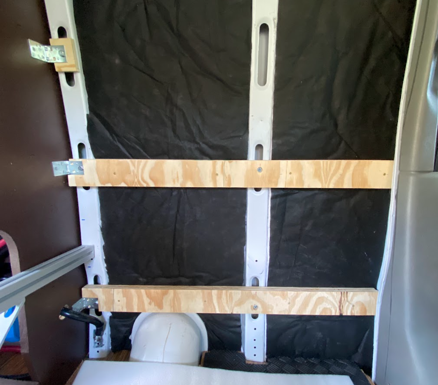 Two wood strips installed on the wall of a cargo van, in front of black insulation.