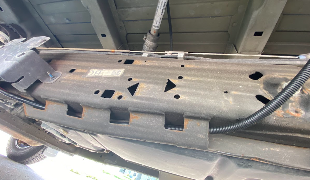 The underside of a van, showing the chassis frame with a wire, inside a protective tube, fastened along the frame.