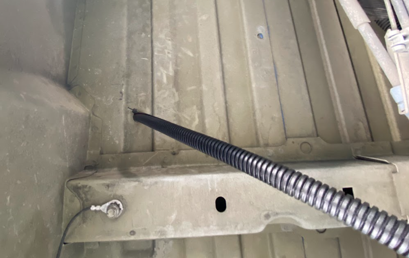 A wire disappearing through the floor of a van, as viewed from underneath the vehicle.