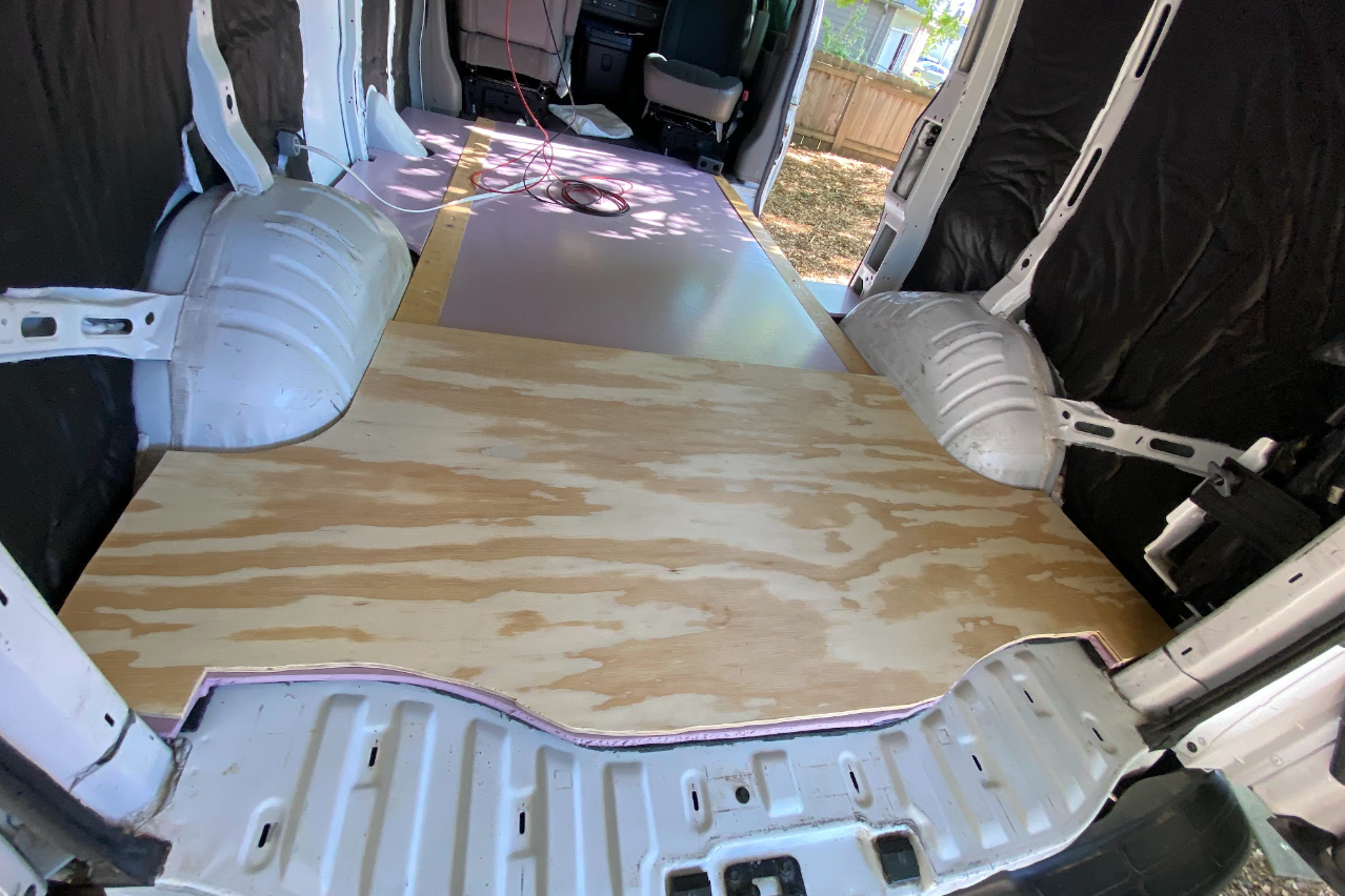 A view inside a cargo van from the rear, with a piece of plywood cut to fit the last few feet.