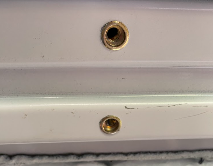 A close up of two threaded inserts in the white metal roof of a van.
