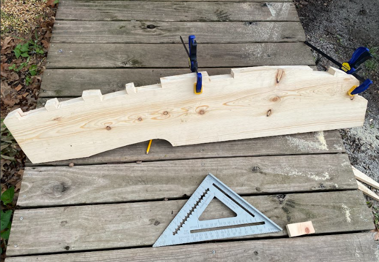 Two boards clamped together. Several notches have been cut along the edge of the boards so that cross members can fit into the notches.