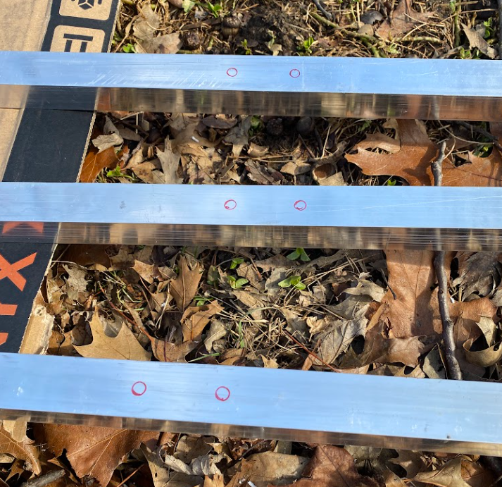 Three aluminum channels with holes marked in red sharpie.