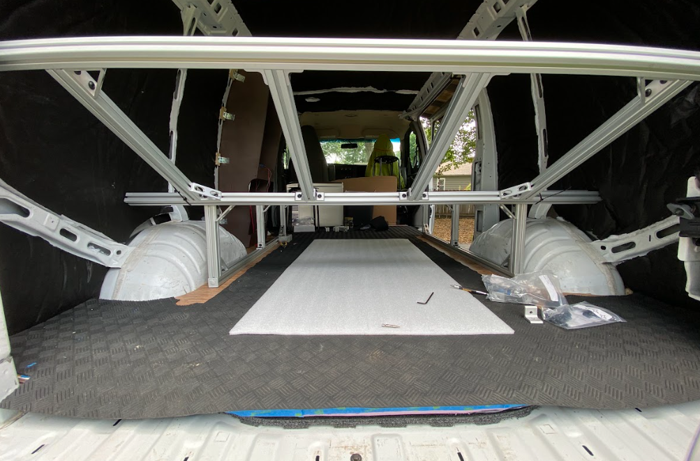 An aluminum bed frame inside a cargo van; view from the rear doors.