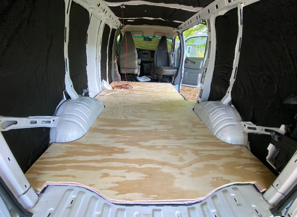 A view from the rear of the interior of a cargo van with a plywood floor.