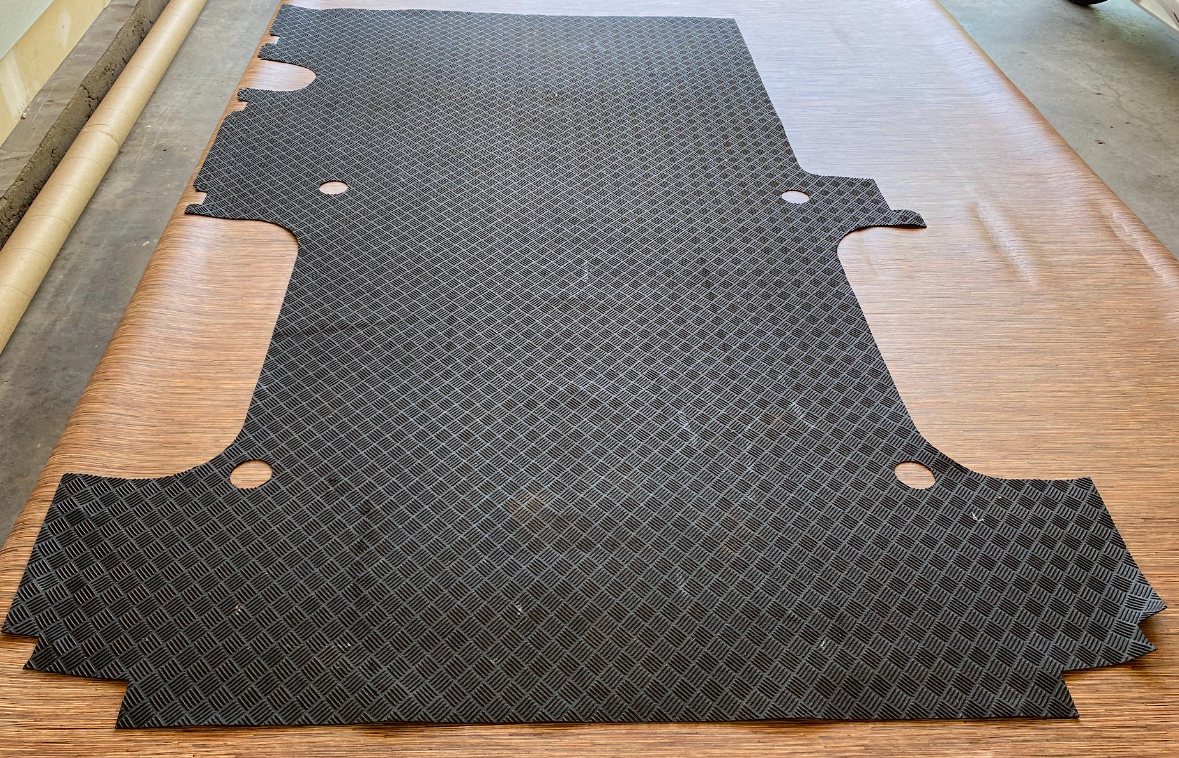 A wood-look vinyl flooring piece with a rubber mat in the shape of a cargo van floor on top.