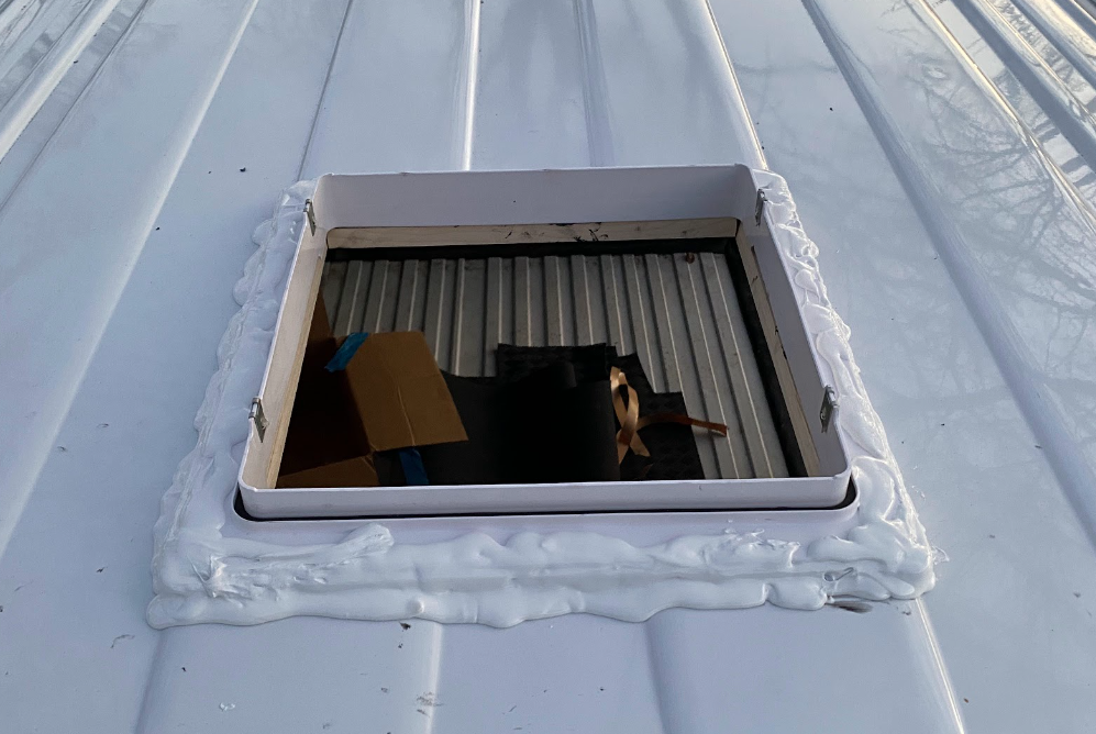 The hole from the outside, with a white frame installed and coated around the border with a sloppy application of white goopy sealant.