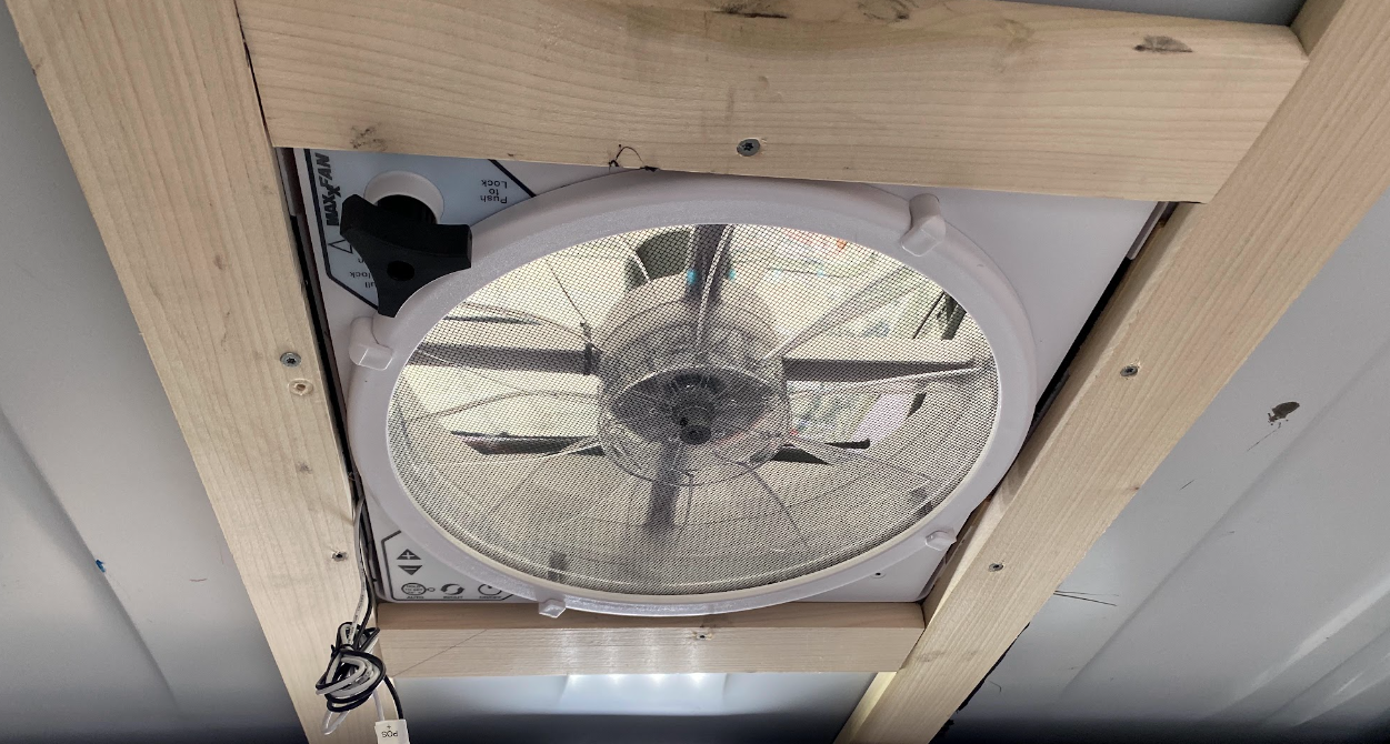 A vent fan viewed from underneath, inside the van, with a wood frame around it.