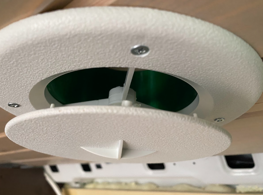 A close-up view of the vent cover, through which a glimpse of the green duct can be seen.