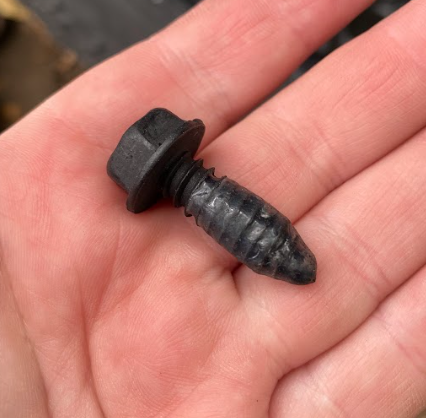 A hand holding a screw with a layer of wax on it.